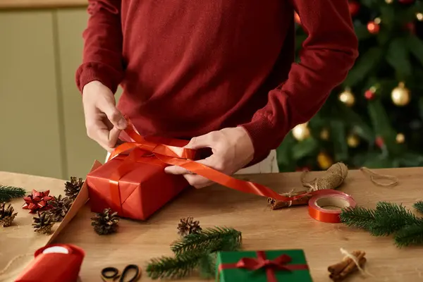 Un joven ata una cinta vibrante alrededor de un regalo rojo en medio de vítores y decoraciones navideñas. - foto de stock