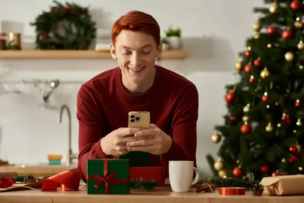 A young man in a festive setting smiles as he interacts with his smartphone during Christmas. — Stock Photo