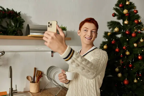 A joyful young man enjoys a warm drink and captures a fun moment during the holiday season. — Stock Photo