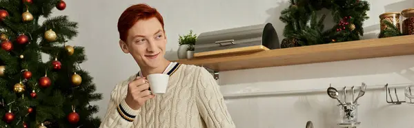A cheerful young man with red hair savors a warm drink amid festive decorations. — Stock Photo