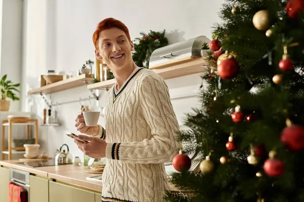 A young man smiles joyfully as he savors coffee amidst festive holiday decorations. — Stock Photo