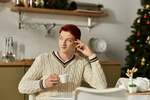 A young man relaxes with a warm drink in a cozy, decorated room filled with holiday cheer. — Stock Photo