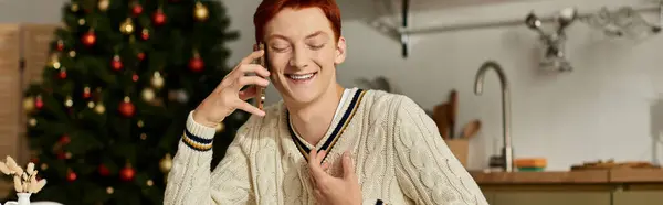 A smiling young man celebrates the holidays by chatting happily on his phone in a stylish kitchen. — Stock Photo