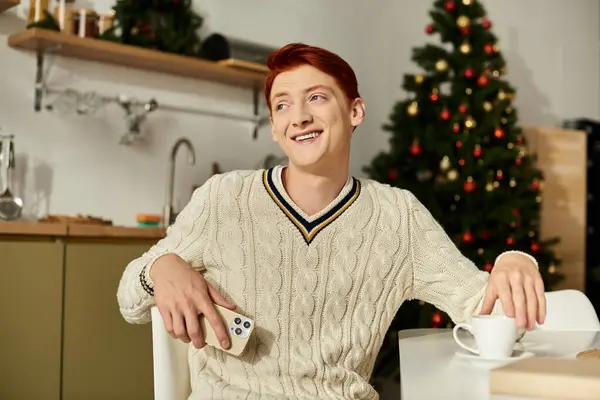 This young man is smiling happily while surrounded by Christmas decorations and a warm drink. — Stock Photo