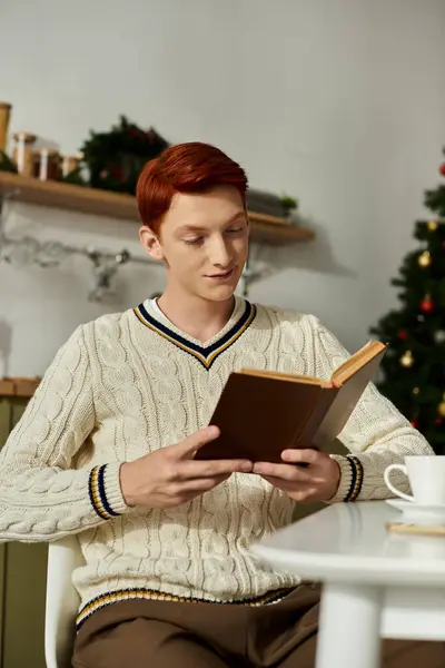 Молодой человек сидит удобно, потерявшись в книге, окруженный праздничными украшениями. — стоковое фото