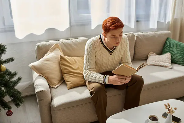 A young man relaxes on a sofa, engrossed in his book amid festive decorations. — Stock Photo