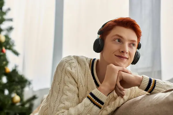 The young man with vibrant hair relaxes on the sofa, lost in joyful Christmas tunes. — Stock Photo
