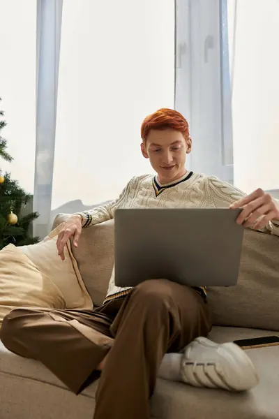 Pendant la saison de Noël, un jeune homme aime naviguer sur son ordinateur portable tout en se relaxant. — Photo de stock