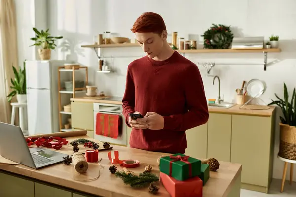 A young man in a red sweater is engaged with his phone while surrounded by Christmas decorations. — Stock Photo