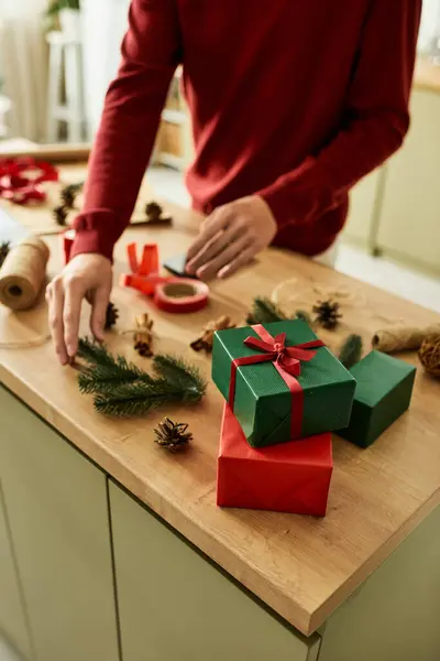 El joven envuelve cuidadosamente los coloridos regalos de Navidad mientras está rodeado de decoraciones navideñas.. - foto de stock