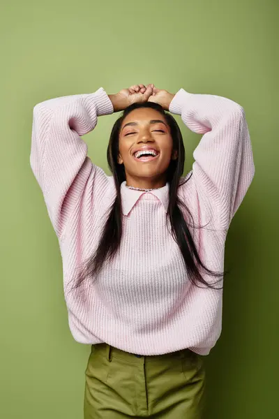 Wearing cozy fashion, a young woman expresses happiness while posing playfully against a green wall — Stock Photo