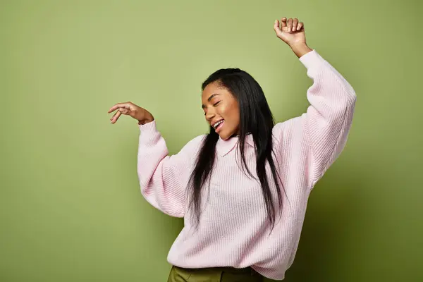 Una joven baila alegremente en una elegante moda otoñal sobre un fondo verde. - foto de stock