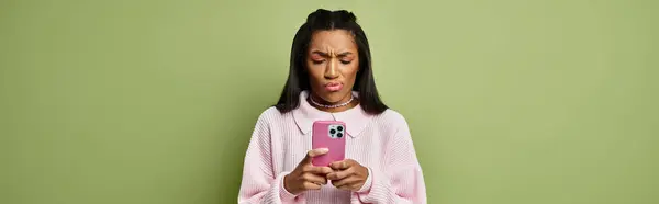 A stylish young woman reacts with curiosity as she looks at her phone against a green backdrop. — Stock Photo