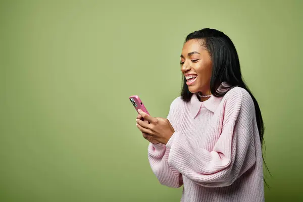 A young woman smiles brightly as she texts on her phone, dressed warmly for autumn. — Stock Photo
