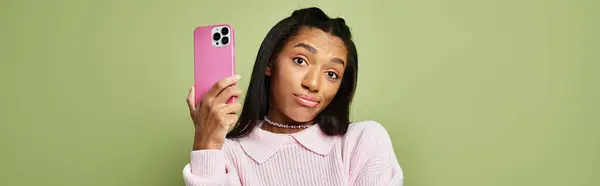 A stylish young woman with a playful expression holds a pink phone, displaying vibrant autumn vibes. — Stock Photo