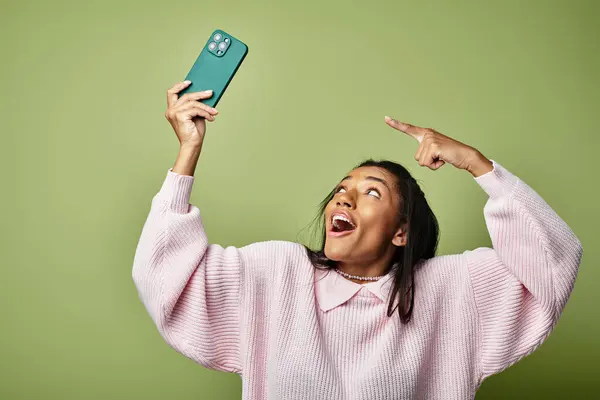 A young woman joyfully poses with her phone, showcasing her stylish outfit and vibrant demeanor. — Stock Photo