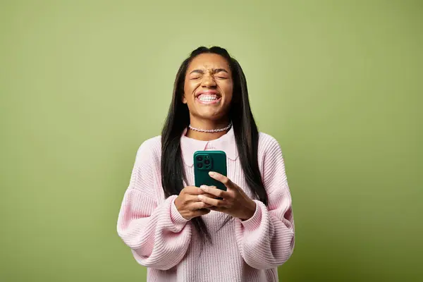 The young woman smiles brightly while engaging with her phone in warm autumn style. — Stock Photo