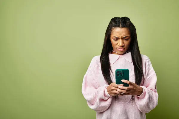 A young woman in stylish warm clothes is focused on her smartphone, lost in thought. — Stock Photo