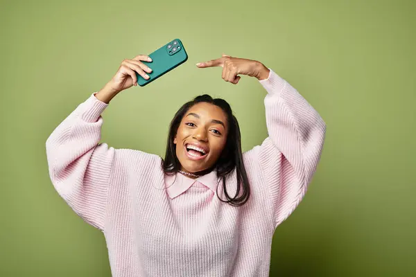 A cheerful young woman shows excitement while holding her smartphone above her head with joy. — Stock Photo