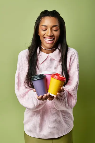 The joyful young woman holds three vibrant coffee cups, dressed in stylish and warm autumn fashion. — Stock Photo