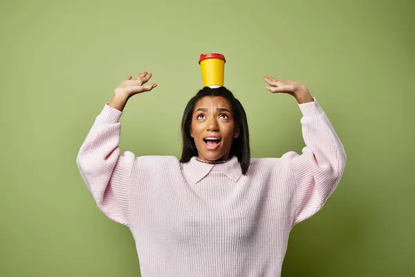 A cheerful woman balances a bright cup on her head while wearing autumn clothes. — Stock Photo