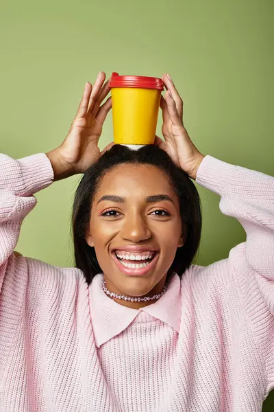 A cheerful young woman balances a vibrant cup on her head, smiling joyfully in cool weather. — Stock Photo