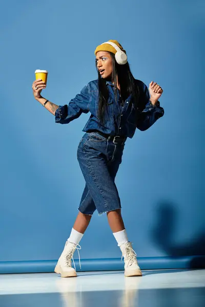 A fashionable young woman dances joyfully while holding a coffee cup, dressed for autumn. — Stock Photo