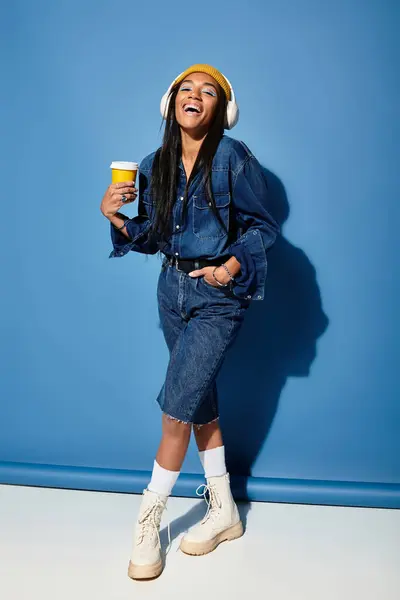 Una joven alegre vestida con un atuendo de otoño de moda toma una bebida caliente, irradiando felicidad. - foto de stock