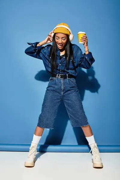 A young woman is joyfully dancing with a drink in hand while wearing trendy autumn clothing. — Stock Photo