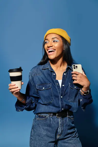 A vibrant young woman smiles with a coffee cup and smartphone, dressed in cozy autumn fashion. — Stock Photo