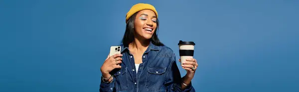 A cheerful young woman, dressed in autumn layers, holds a coffee cup and phone, radiating happiness. — Stock Photo