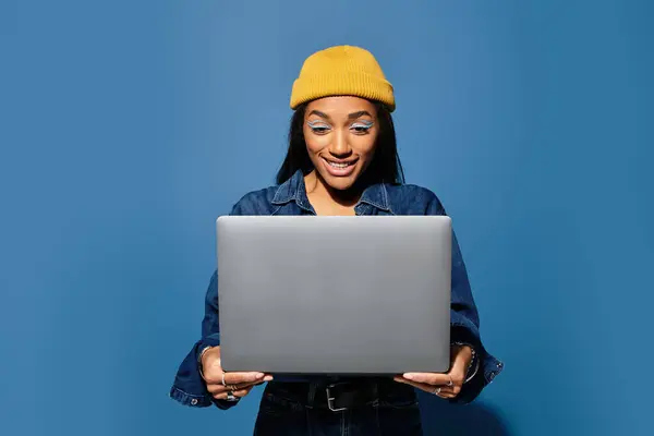A young woman in a stylish outfit smiles at her laptop in a cheerful setting. — Stock Photo