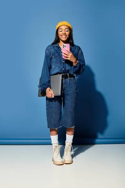 A young woman with a warm smile showcases her trendy autumn outfit while holding a phone. — Stock Photo