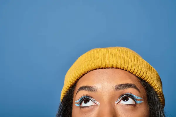 A young woman in a cozy yellow beanie admires the sky, showcasing her unique eye makeup. — Stock Photo