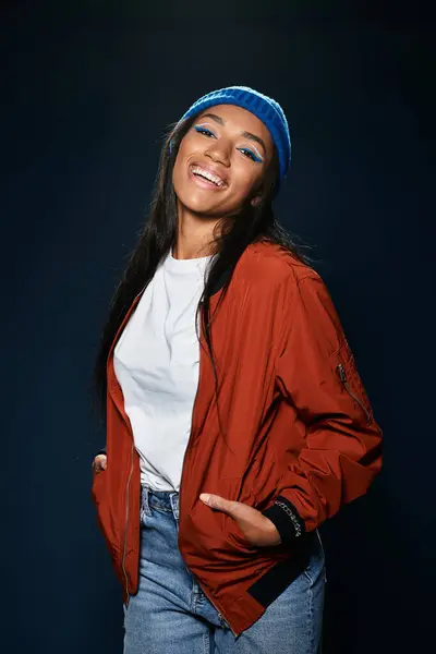 A young woman radiates confidence in warm autumn attire while standing against a dark backdrop. — Stock Photo