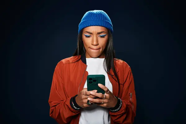 A fashionable young woman in autumn attire is engaged with her smartphone, deep in thought. — Stock Photo
