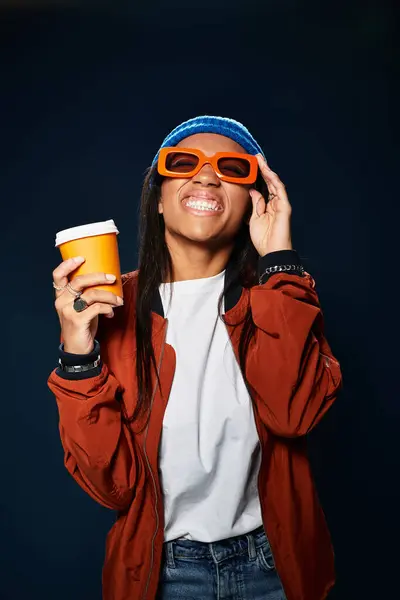 The young woman, wearing orange sunglasses, smiles brightly while holding a warm drink. — Stock Photo