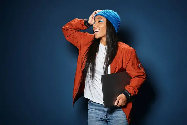 A joyful young woman in warm autumn fashion smiles and holds a laptop under her arm. — Stock Photo