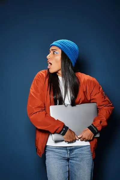 A young woman wearing cozy fall clothing looks surprised while clutching a laptop. — Stock Photo