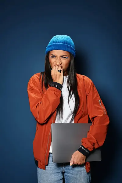 A stylish young woman wearing a cozy jacket and beanie looks worried while gripping her laptop. — Stock Photo