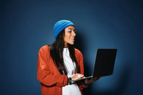 Wearing a trendy outfit, a young woman smiles while using her laptop, embracing autumn style. — Stock Photo