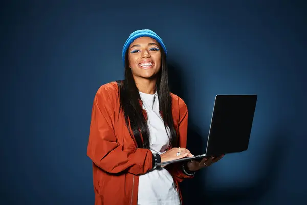 A cheerful young woman dressed in autumn layers joyfully works on her laptop indoors. — Stock Photo