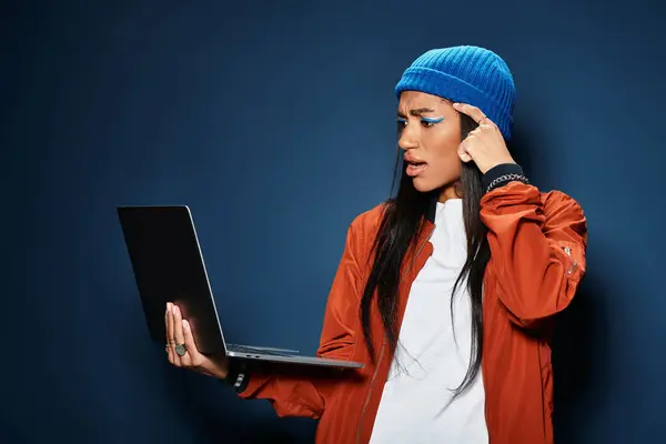 A young woman in warm fall clothing deeply engages with her laptop, expressing curiosity. — Stock Photo