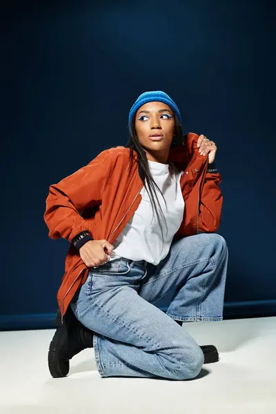 A fashionable young woman showcases her autumn style while kneeling gracefully in a studio setting. — Stock Photo