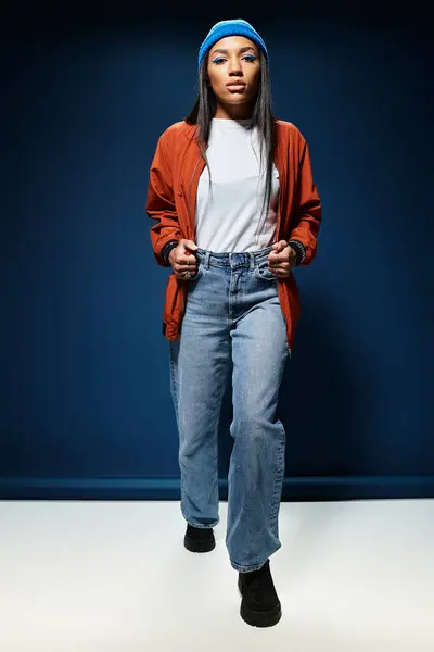 A young woman strolls confidently, flaunting stylish autumn attire against a deep blue backdrop. — Stock Photo