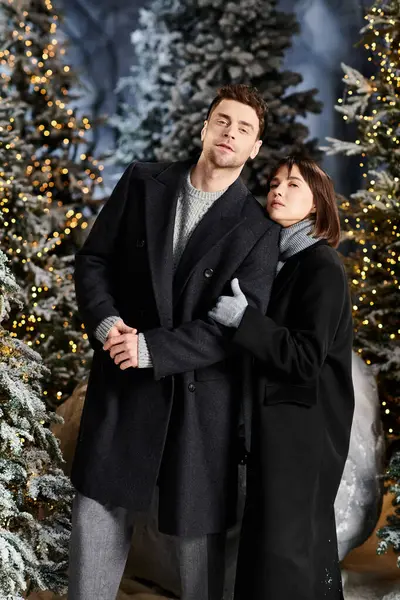 A joyful couple in cozy winter coats embraces near snow-covered pine trees, celebrating the festive season. — Stock Photo