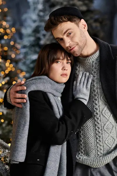 A couple in warm winter coats cuddles affectionately by the snowy pine trees, celebrating the festive season. — Stock Photo