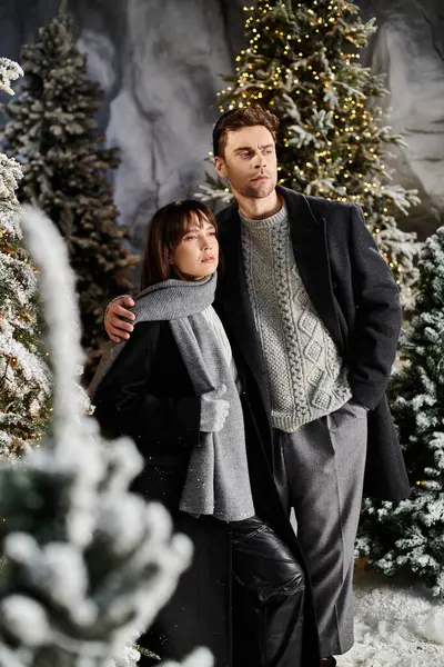 Couple embraces in winter coats, sharing festive joy amidst snow-covered pine trees. — Stock Photo