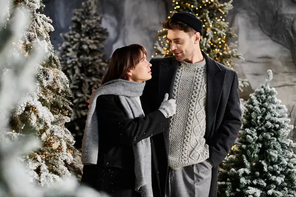 A couple enjoys a cozy moment in winter coats amidst snow-covered pines, capturing the festive spirit. — Stock Photo