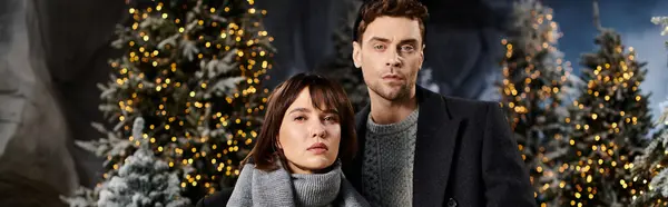 A couple wrapped in winter coats near snow-covered pine trees during the holidays. — Stock Photo